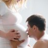 Фотосессия беременных в студии, муж целует животик жены на белом фоне